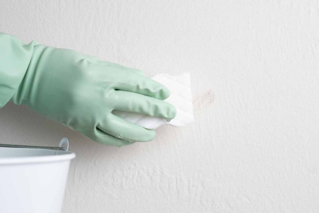 Hand wiping a stain off a white painted wall with a cloth during interior wall cleaning