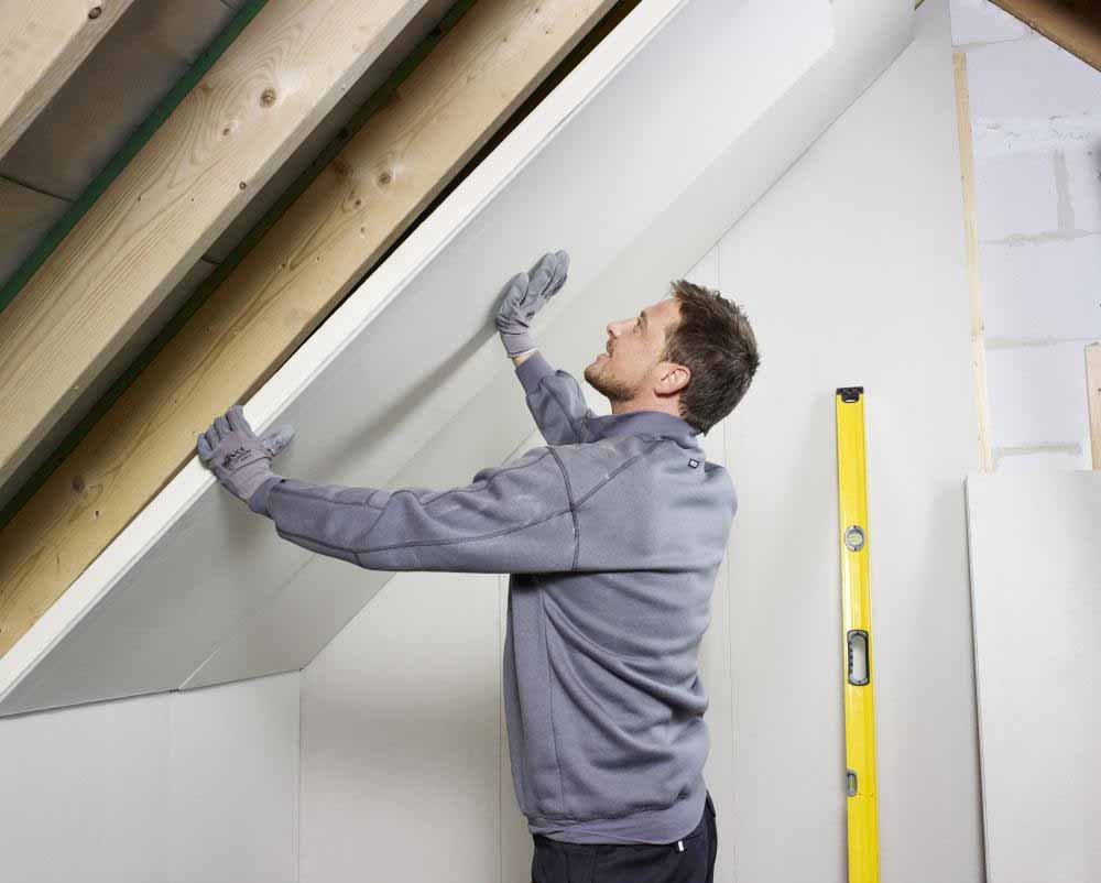 Tradesman installing insulated plasterboard on a sloped interior wall during plasterboard installation in a New Zealand home