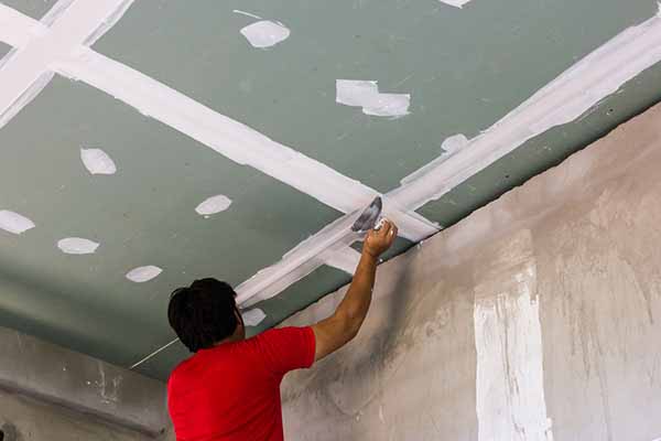 Stopper applying compound over taped joints and screw heads on a plasterboard ceiling