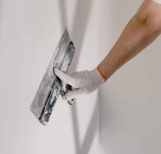 Tradesperson skimming a smooth finishing coat across a plasterboard wall with a taping knife